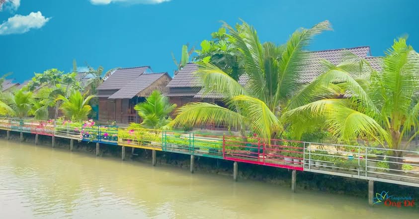 Dãy nhà gỗ homestay ven sông với lan can hoa nhiều màu tại Làng du lịch sinh thái Ông Đề